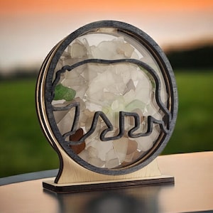 May include: A wooden bear silhouette with a round glass insert filled with sea glass. The sea glass is a mix of white, green, and brown.