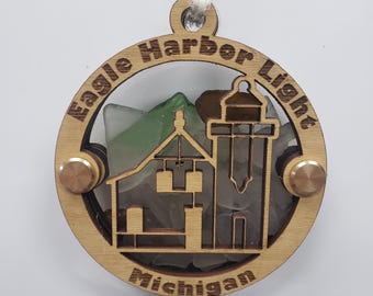 Könnte beinhalten: Runder Holzschmuck mit Leuchtturm-Design, der Text lautet "Eagle Harbor Light Michigan". Der Schmuck hat einen Leuchtturmausschnitt und ist mit Meerglas gefüllt. Er wird von einer weißen Schnur gehalten.