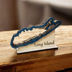 May include: A wooden cutout of Long Island, New York, painted blue and mounted on a white base. The base has the words "Long Island" engraved on it.