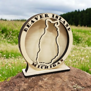 May include: A wooden cutout of Beaver Island, Michigan. The island is outlined in black and the words "Beaver Island" and "Michigan" are written around the perimeter.
