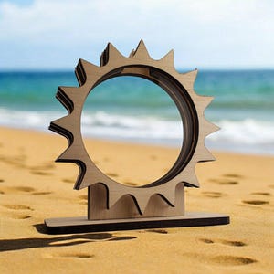 May include: A wooden sun-shaped sculpture with a circular opening in the center. The sculpture is standing on a wooden base and is on a sandy beach.