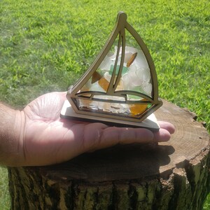May include: A wooden sailboat figurine with a clear resin base filled with colorful sea glass. The sailboat is sitting on a tree stump.