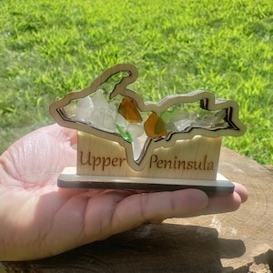 May include: Wooden cutout of the Upper Peninsula of Michigan with colorful glass pieces inside. The base of the cutout is engraved with the words "Upper Peninsula".