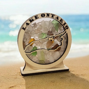 May include: A wooden cutout of Lake Ontario filled with colorful sea glass. The cutout is on a wooden base and the text "LAKE ONTARIO" is written around the edge.