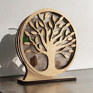 May include: A wooden tree of life sculpture with a circular base. The tree is cut out and has a hollow center filled with small pieces of glass. The base is stained a dark brown color.