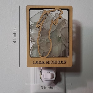 May include: A wooden night light shaped like the outline of Lake Michigan. The lake is filled with clear glass pieces. The night light is 4 inches tall and 3 inches wide. It says "LAKE MICHIGAN" on the bottom.