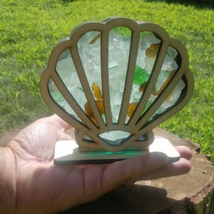 May include: A wooden seashell sculpture with a clear glass base filled with sea glass in shades of green, white, and amber.