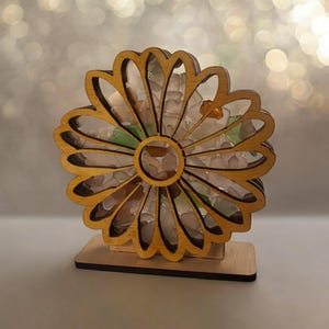 May include: A wooden flower-shaped sculpture with a clear resin center filled with colorful sea glass. The sculpture is on a wooden base.