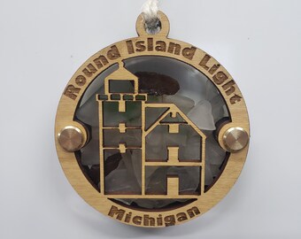Könnte beinhalten: Runder Holzschmuck mit Leuchtturm-Design und dem Text "Round Island Light Michigan". Der Schmuck hat eine transparente Mitte, die mit Meeresglas gefüllt ist und mit messingfarbenen Nieten zusammengehalten wird. Eine weiße Schnur ist zum Aufhängen befestigt.