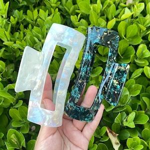 May include: Two hair clips, one white with iridescent flecks and one dark green with gold flecks.