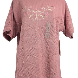 May include: Dusty pink short-sleeved sweater with floral embroidery. The sweater has a textured knit pattern and a series of "Small" tags. The embroidery features pink flowers and gold-coloured stems.