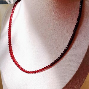 May include: A red gemstone necklace with small, round beads. The necklace is displayed on a white mannequin bust.