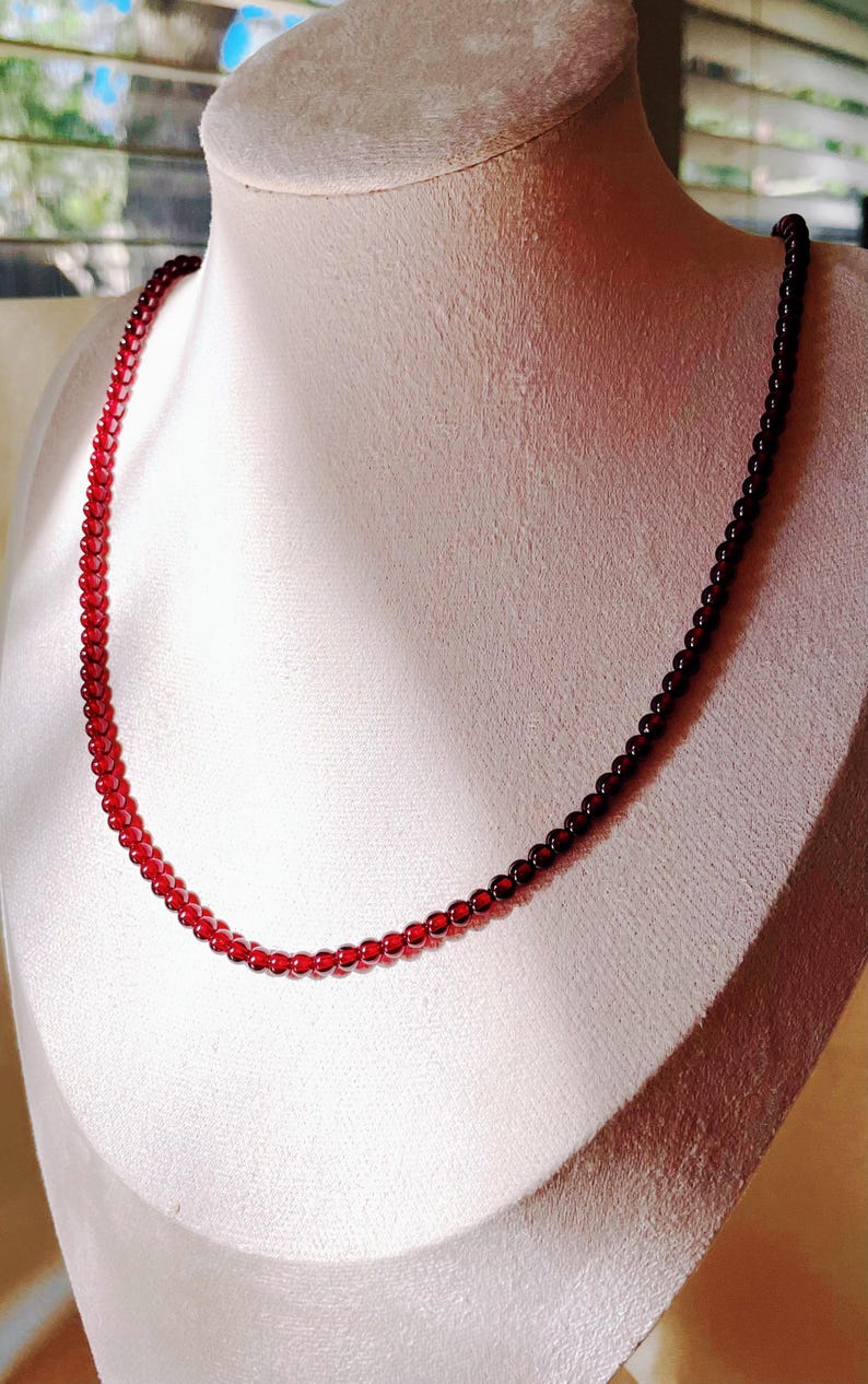 May include: A red gemstone necklace with small, round beads. The necklace is displayed on a white mannequin bust.