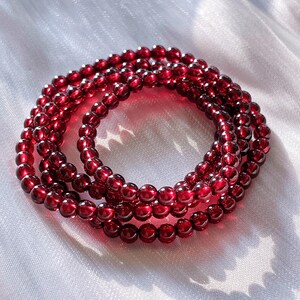 May include: A red garnet beaded bracelet with multiple strands. The bracelet is made of small, round beads that are strung together to create a long, flowing design.