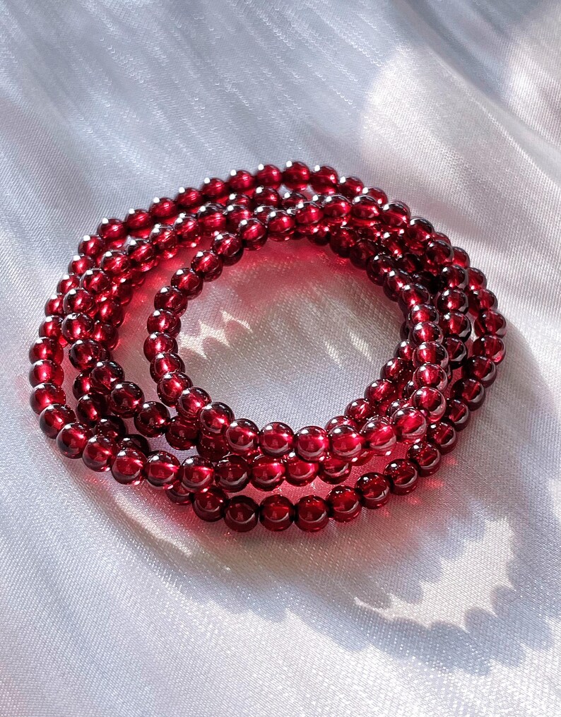 May include: A red garnet beaded bracelet with multiple strands. The bracelet is made of small, round beads that are strung together to create a long, flowing design.