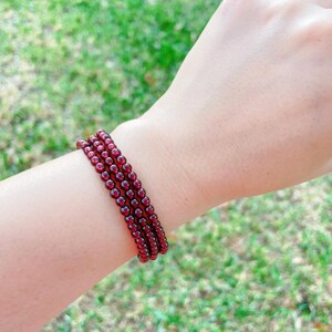 May include: A stack of four red garnet beaded bracelets on a person's wrist.