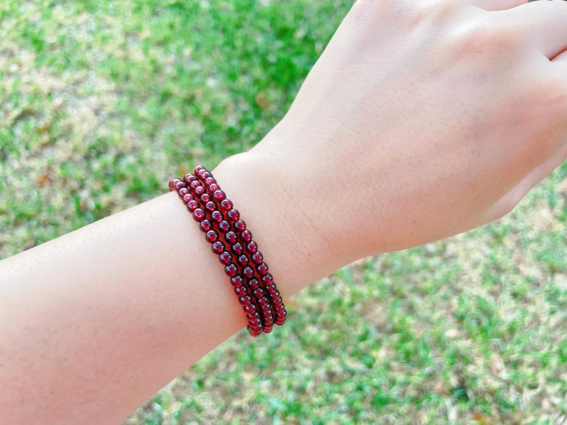May include: A stack of four red garnet beaded bracelets on a person's wrist.