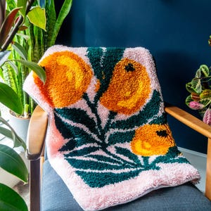May include: A pink and green throw blanket with a tufted design featuring orange lemons and green leaves.