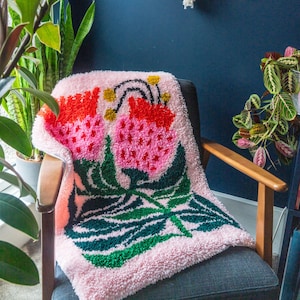 May include: A pink, fluffy throw blanket with a colorful floral design. The design features two large pink flowers with red and yellow accents, surrounded by green leaves.