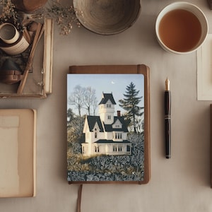 May include: A still-life arrangement featuring a notebook with a house illustration, a fountain pen, a cup of tea, and a teapot. The notebook has a brown cover and a picture of a white house with black roof. Other items include a small bowl, a candle, and a vintage clock.