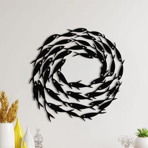 May include: Black metal wall art featuring a circular design of fish swimming in a circle. The fish are all facing the same direction and are arranged in a spiral pattern.