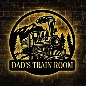 May include: Black metal sign with a silhouette of a train engine and a mountain scene. The sign reads "DAD'S TRAIN ROOM".