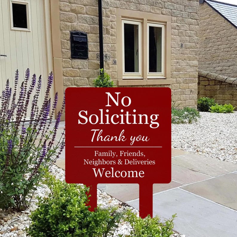 May include: A rectangular dark red garden sign with white text that reads No Soliciting Thank you, followed by Family, Friends, Neighbors & Deliveries Welcome. The sign features two stakes at the bottom for insertion into the ground.