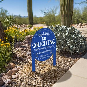 May include: A blue oval yard sign with white text that reads: Absolutely NO SOLICITING, FRIENDS, FAMILY & DELIVERIES always welcome. If that's not you, Do not knock or ring bell. The sign is mounted on two blue stakes in the ground.