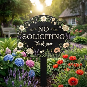 May include: A black, arched garden sign on a stake featuring the white text NO SOLICITING Thank you. The sign is decorated with a colorful botanical border of white, pink, and orange flowers, green leaves, and small butterflies.