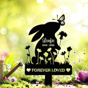 May include: Black metal garden stake with a rabbit silhouette, butterfly, and flowers. The text "Loafie 2016-2023" is inscribed on the rabbit. The stake also includes the words "FOREVER LOVED" with heart accents, suitable for memorial gardens.