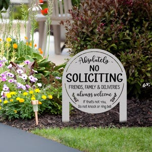 May include: A round, light gray metal garden sign with two stakes. The text reads: Absolutely NO SOLICITING. FRIENDS, FAMILY & DELIVERIES always welcome. If that's not you, Do not knock or ring bell. The sign features black lettering and leaf accents.