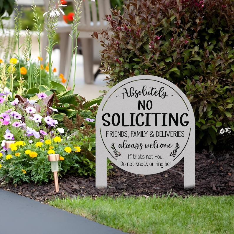 May include: A round, light gray metal garden sign with two stakes. The text reads: Absolutely NO SOLICITING. FRIENDS, FAMILY & DELIVERIES always welcome. If that's not you, Do not knock or ring bell. The sign features black lettering and leaf accents.