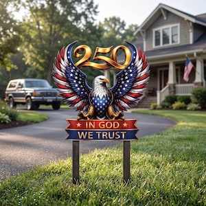 以下が含まれることがあります： アメリカ国旗の色を使用した、翼を広げたアメリカのハクトウワシが描かれた愛国的なガーデンステーク。ワシの上には数字の「250」があり、バナーには「IN GOD WE TRUST」と書かれています。芝生の庭に設置されています。