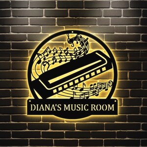 May include: A black metal sign with a harmonica and musical notes, illuminated with warm yellow light. The sign reads "Diana's Music Room".