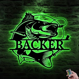 May include: Black metal sign with a fish design and the name "BACKER" in a horizontal bar. The sign is illuminated with green LED lights, creating a glowing effect. A remote control is visible in the bottom right corner.