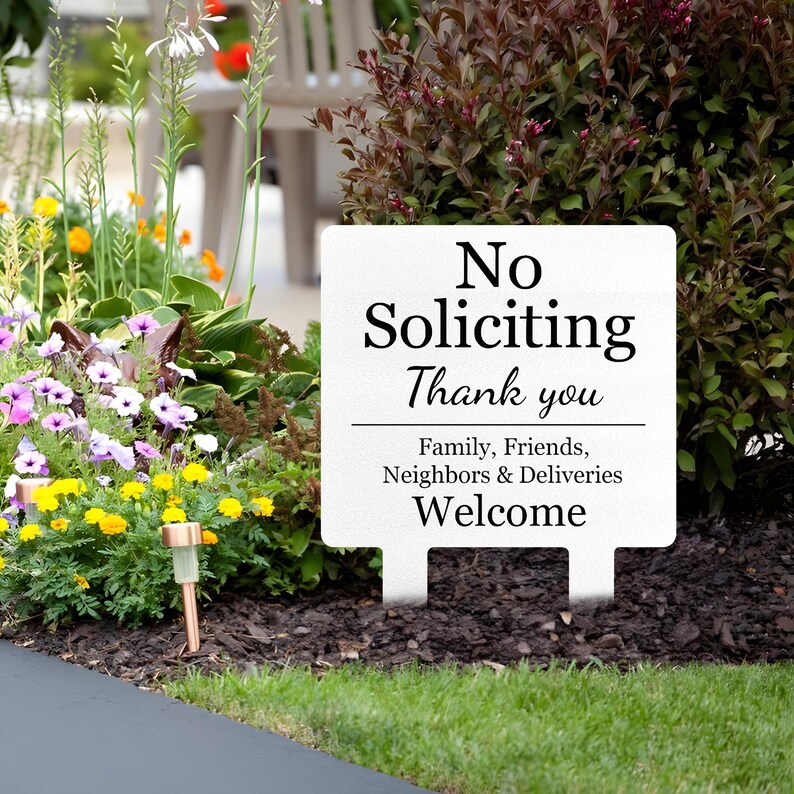 May include: A white rectangular yard sign with black text that reads No Soliciting Thank you, followed by a horizontal line and the text Family, Friends, Neighbors & Deliveries Welcome. The sign has two stakes at the bottom.