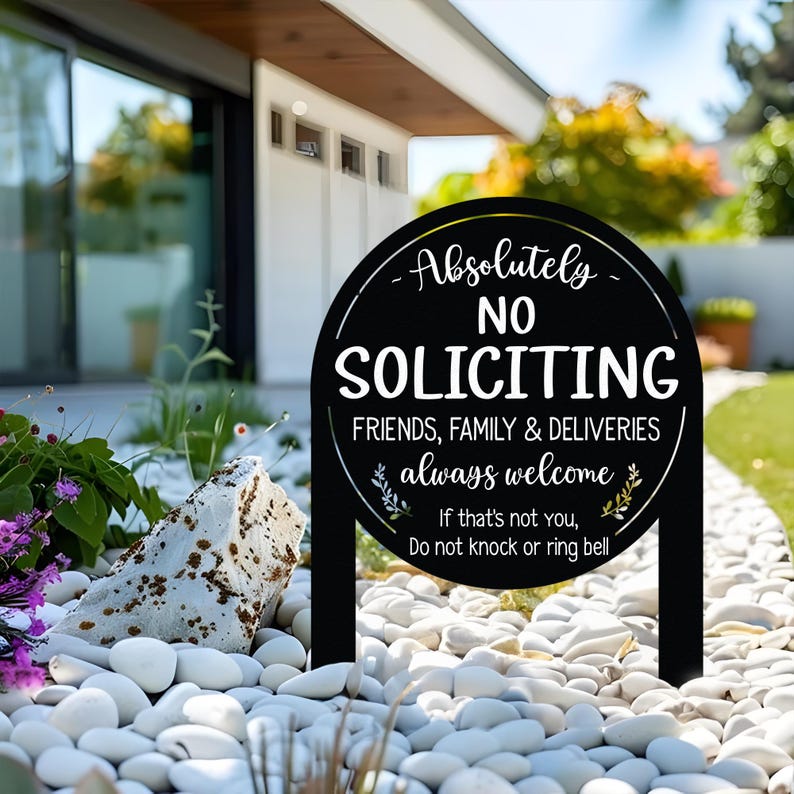 May include: A black round yard sign with white text that reads Absolutely NO SOLICITING FRIENDS, FAMILY & DELIVERIES always welcome. If that's not you, Do not knock or ring bell. The sign features two stakes and decorative leaf graphics.