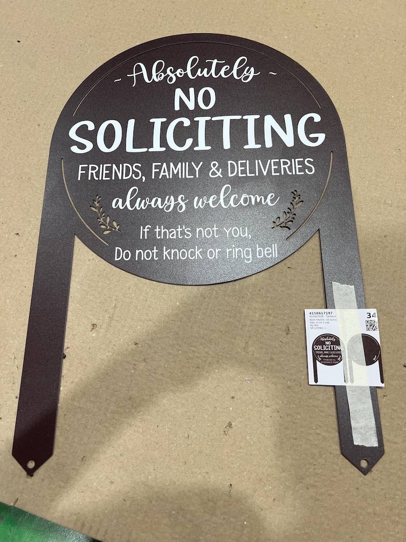 May include: A dark brown metal yard sign with an arched top and two stakes. The text reads: Absolutely NO SOLICITING, FRIENDS, FAMILY & DELIVERIES always welcome, If that's not YOU, Do not knock or ring bell. A small product label is attached.
