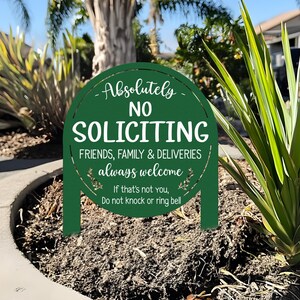 May include: A dark green, round, arched yard sign with white text that reads: Absolutely NO SOLICITING, FRIENDS, FAMILY & DELIVERIES always welcome, If that's not you, Do not knock or ring bell. The sign features two stakes for ground insertion.