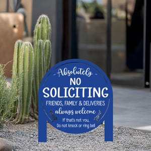 May include: A circular blue metal sign with white text that reads: Absolutely NO SOLICITING. FRIENDS, FAMILY & DELIVERIES always welcome. If that's not you, Do not knock or ring bell. The sign features two legs for ground insertion.