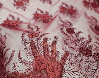 May include: Burgundy floral lace fabric with a delicate pattern of flowers and leaves. The lace has a soft, flowing texture and is perfect for adding a touch of elegance to any project.