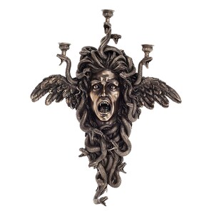 May include: A bronze-coloured wall sconce depicting Medusa's face, with snakes forming her hair. It has three candle holders and two feathered wings. The Medusa face is screaming with its mouth open.