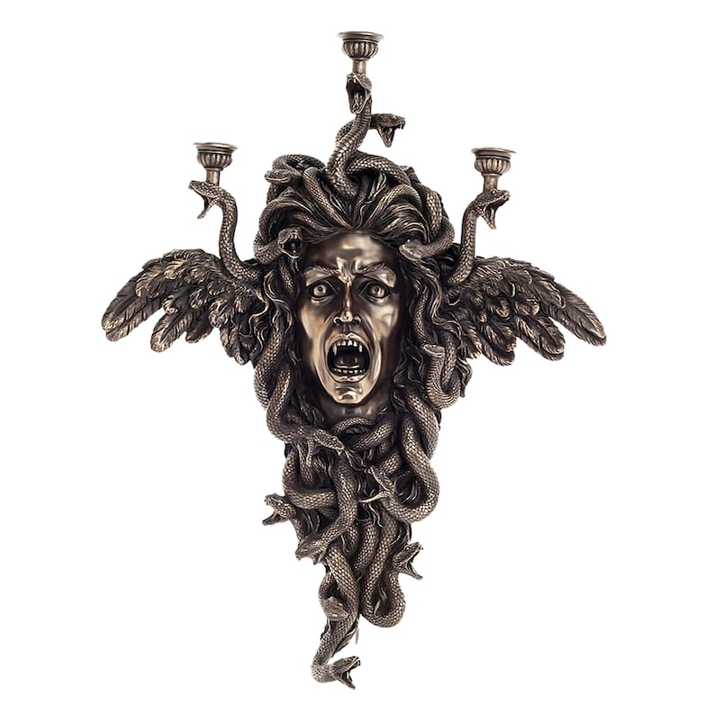May include: A bronze-coloured wall sconce depicting Medusa's face, with snakes forming her hair. It has three candle holders and two feathered wings. The Medusa face is screaming with its mouth open.