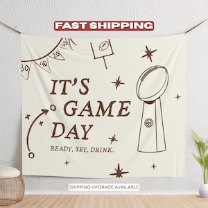 Può includere: Arazzo color crema con testo e illustrazioni marroni. Le parole "IT'S GAME DAY" sono ben visibili, insieme a un pallone da football, un trofeo e un diagramma di gioco. È inclusa anche la frase "READY, SET, DRINK". Le parole "FAST SHIPPING" sono in alto.
