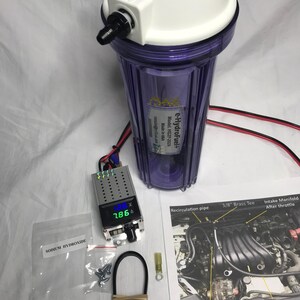 Può includere: Un kit generatore HHO e-Hydrofuel+ composto da un contenitore cilindrico viola con tappo bianco, un'unità display digitale con cifre LED verdi, un sacchetto di idrossido di sodio, viteria, una fascetta nera e uno schema di installazione.