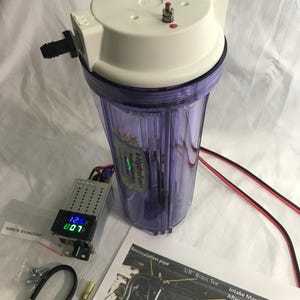 May include: A clear cylindrical hydrogen generator canister with a white top lid, two metal terminals, and a black plastic outlet. It includes a digital voltage and amperage display module, red and black electrical wires, and an instruction sheet.