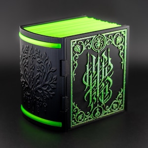May include: A black, book-shaped box with detailed green designs and a glowing green edge. The box has a floral pattern on one side and ornate lettering on the other. The pages inside are bright green.