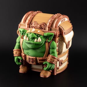 Puede incluir: Un cofre de fantasía con una figura de orco verde integrada. El cofre presenta un aspecto de madera con detalles marrones y beige. El orco tiene una tez verde, correas marrones y una diadema dorada. Artículo decorativo único.
