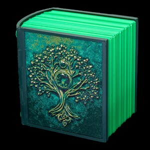 May include: A green book with a gold embossed tree design on the cover. The book is closed and has a spine with multiple ridges.