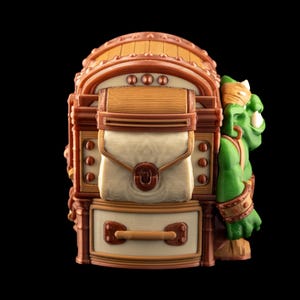 May include: A detailed, fantasy-themed figurine featuring a green orc character leaning against a brown and beige treasure chest. The chest has a hinged lid, a central pouch, and a drawer with a handle. The orc has a gold headband and armbands.